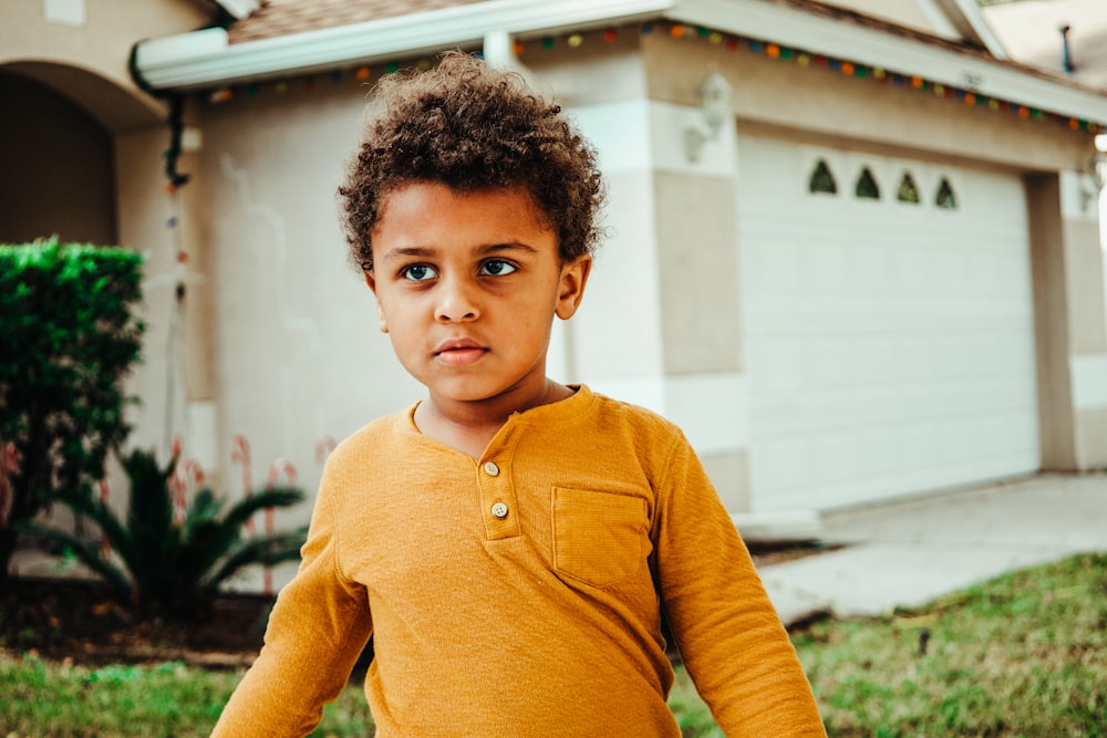 boy in yellow henley long sleeve shirt standing near white building during daytime