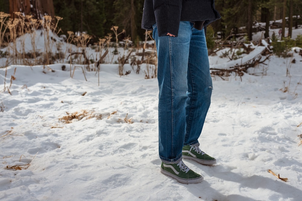 Person in blauer Jeans und schwarzer Jacke, die tagsüber auf schneebedecktem Boden steht