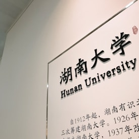A wall with a framed plaque displays the text 'Hunan University' in both Chinese and English. The white background contrasts with the black text, which includes a description in Chinese characters.