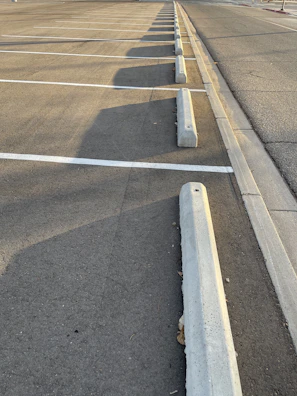 Before and after of a commercial parking lot cleaned and freshly striped under bright sunlight.