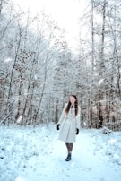 A model wearing a sleek winter coat walking through a frosty forest path with muted blue tones.