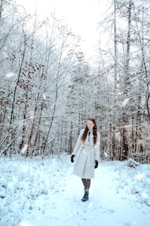 A model wearing a sleek winter coat walking through a frosty forest path with muted blue tones.