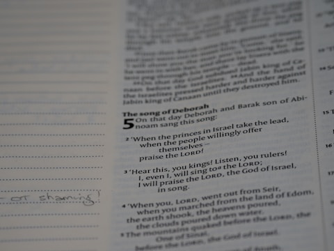 An open book displaying a page with text from 'The Song of Deborah' in a biblical style, featuring verses and numbers. The text is printed in black on an off-white background. There are also lined margins for notes with some handwritten text visible.