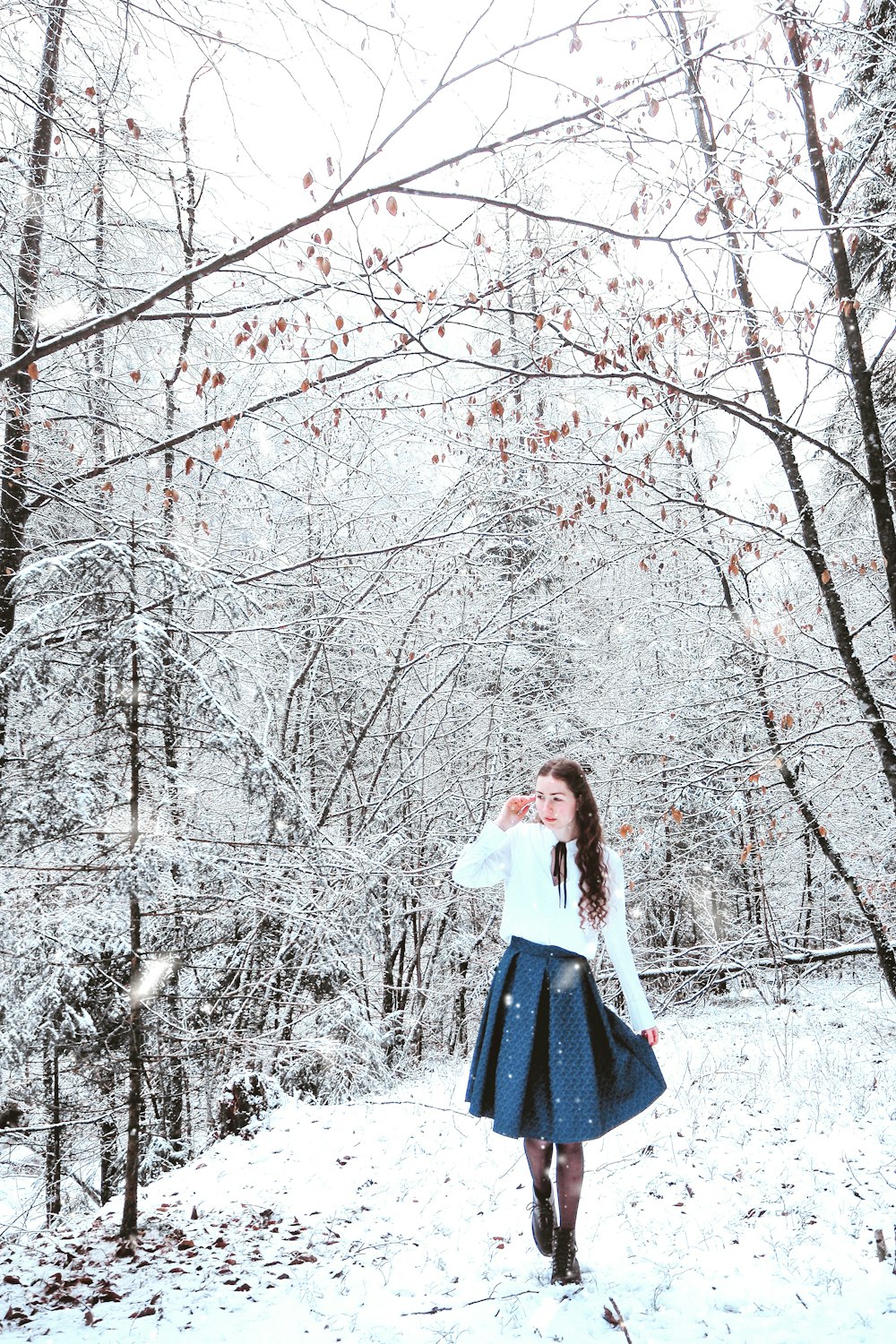 白い長袖シャツと青いスカートを着た女性が、雪に覆われた地面に立っています。