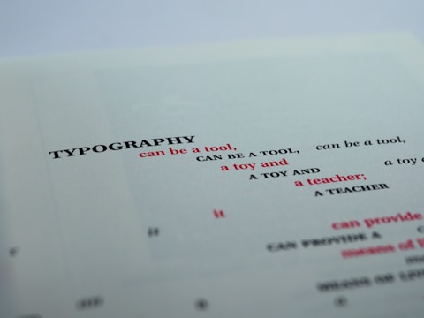 A close-up view of a printed page featuring the word 'TYPOGRAPHY' in bold black letters, followed by several phrases in varying font sizes and colors. The text is creatively arranged with alternating red and black fonts, primarily focusing on the functional and playful aspects of typography.