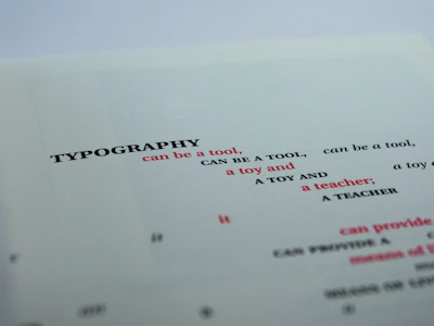 A close-up view of a printed page featuring the word 'TYPOGRAPHY' in bold black letters, followed by several phrases in varying font sizes and colors. The text is creatively arranged with alternating red and black fonts, primarily focusing on the functional and playful aspects of typography.
