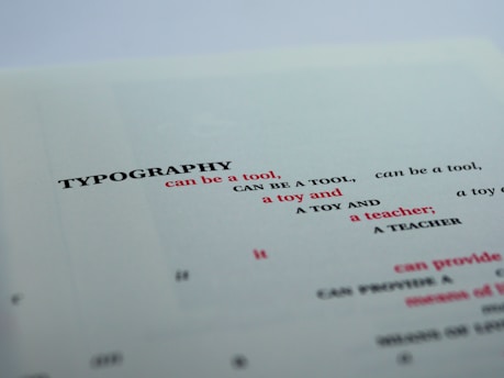 A close-up view of a printed page featuring the word 'TYPOGRAPHY' in bold black letters, followed by several phrases in varying font sizes and colors. The text is creatively arranged with alternating red and black fonts, primarily focusing on the functional and playful aspects of typography.