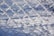 A chain-link fence is covered in frost, with the background showing snow-covered ground and subtle shadows.