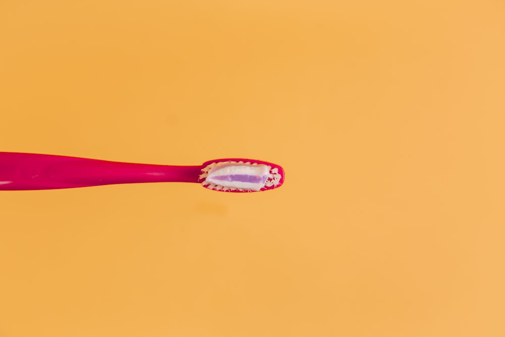 cepillo de dientes rosa y amarillo sobre fondo naranja