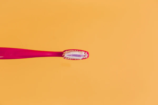 A bright pink toothbrush against a sunny yellow background