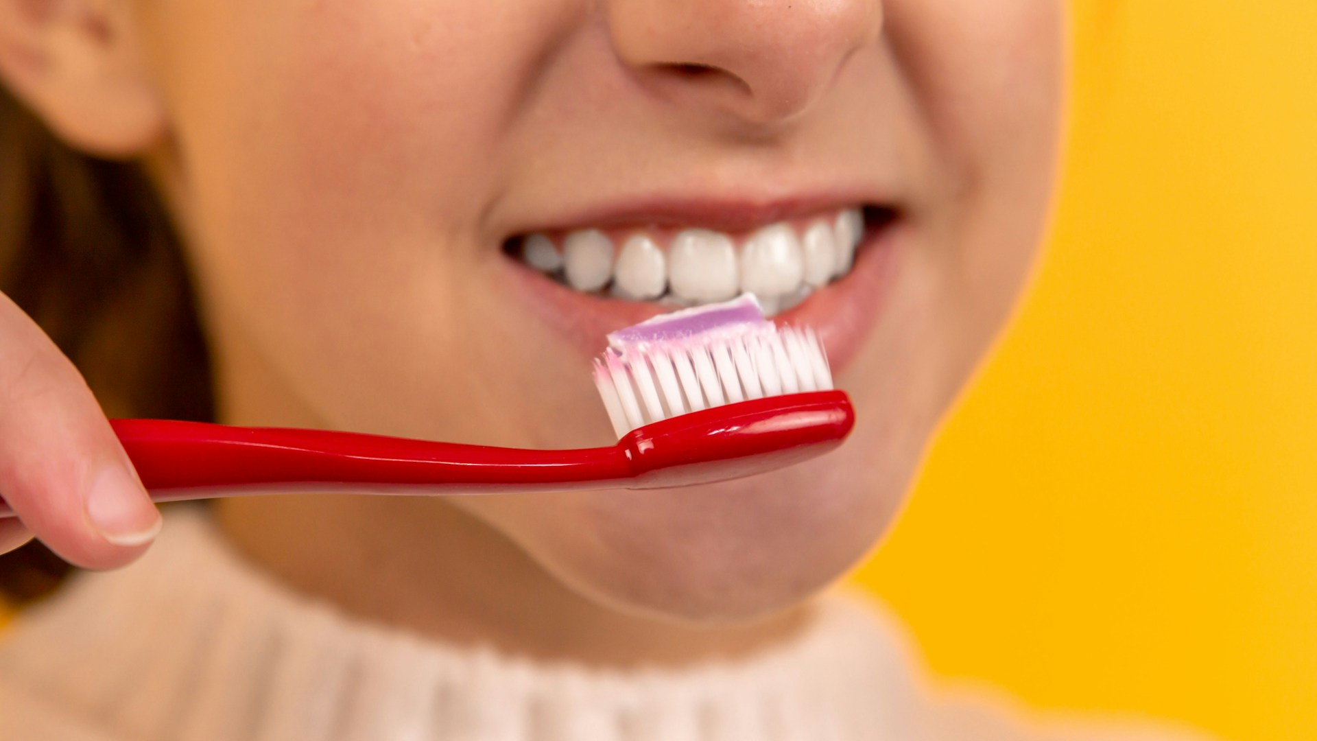 garota escovando os dentes com uma escova vermelha e branca