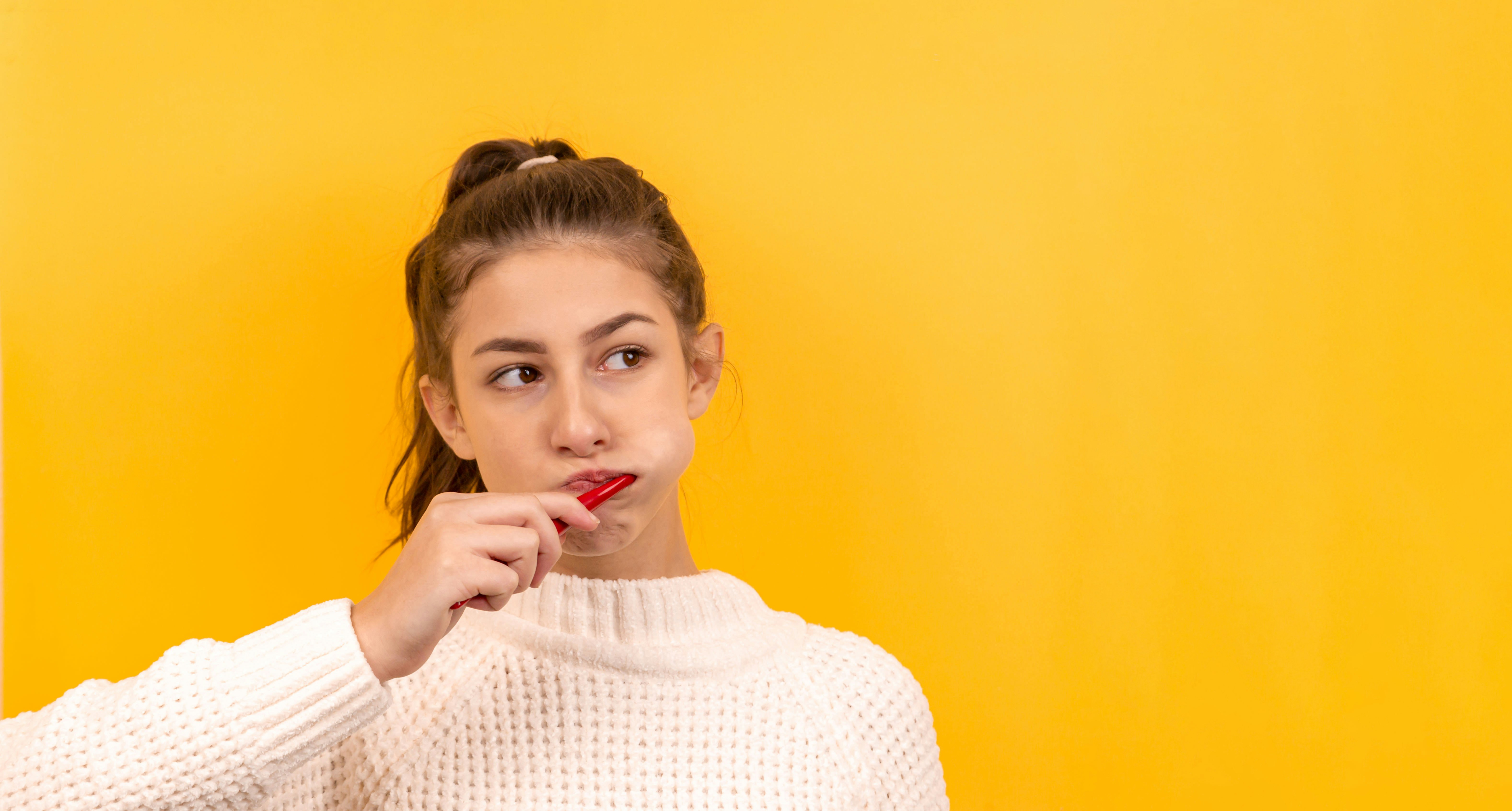 Portrait of a beautiful girl on a yellow background, who is brushing her teeth and is thinking about something. Place for an inscription. Portrait. Dentistry