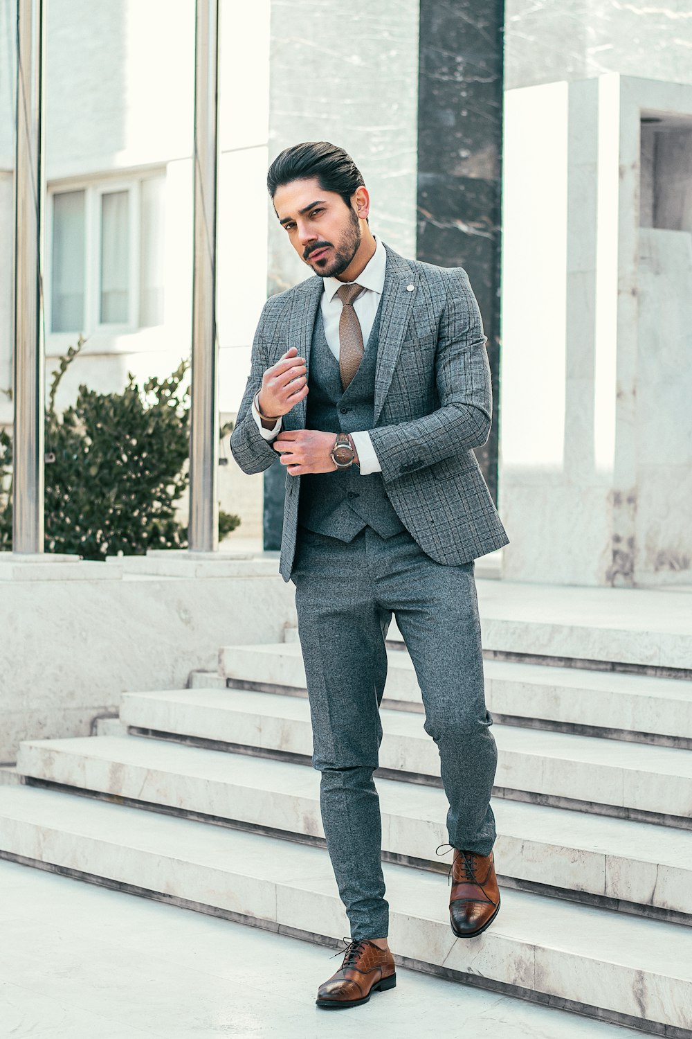 Hombre con chaqueta de traje gris y pantalones negros de pie en una escalera blanca