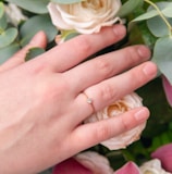 person wearing gold wedding band holding white rose