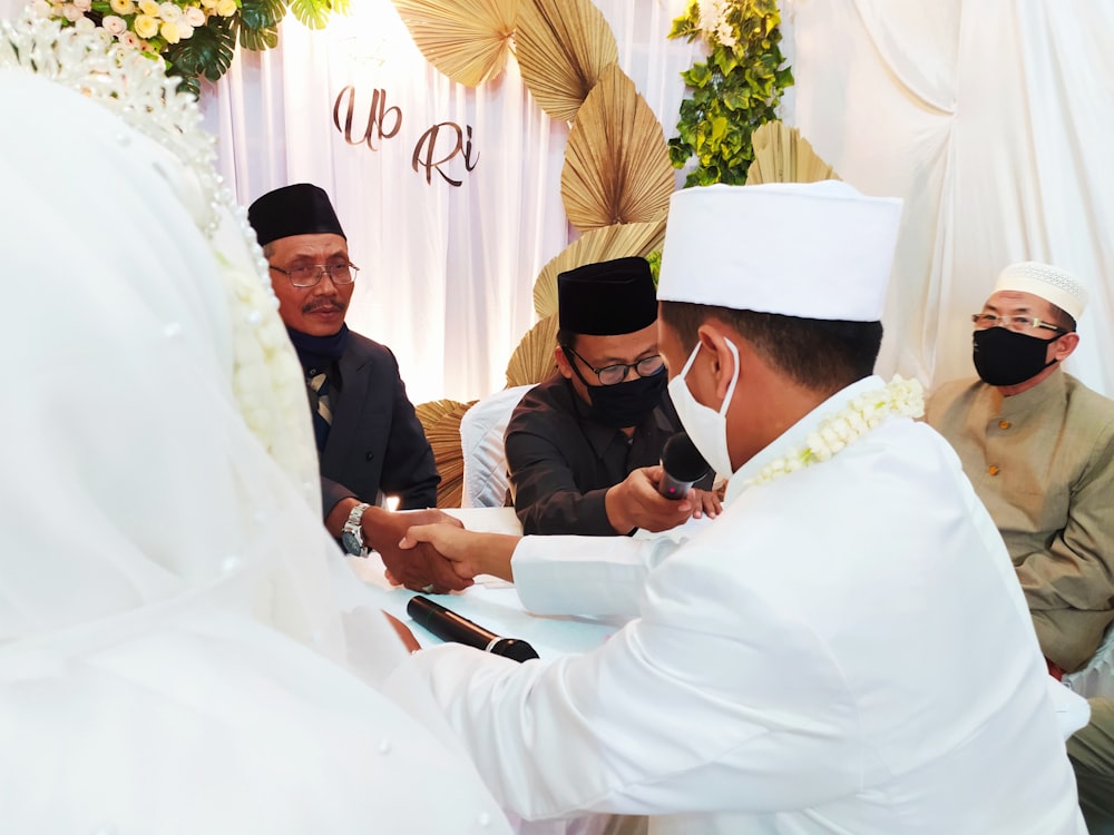 man in black suit sitting beside man in white thobe