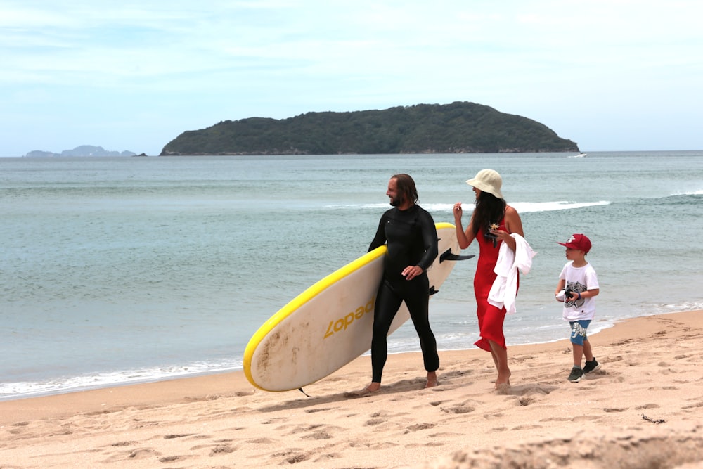 uomo e donna che tengono la tavola da surf gialla che cammina sulla spiaggia durante il giorno