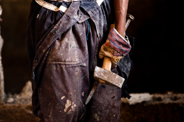 Hand wearing a work glove holding a sturdy hammer against a blurred background.