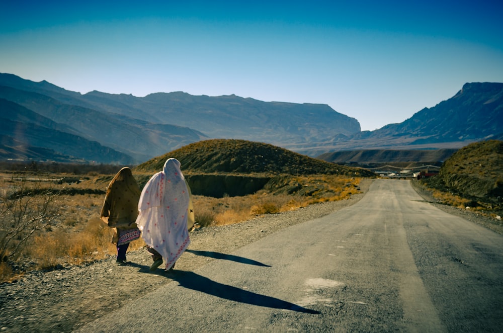 person in white hoodie walking on gray asphalt road during daytime