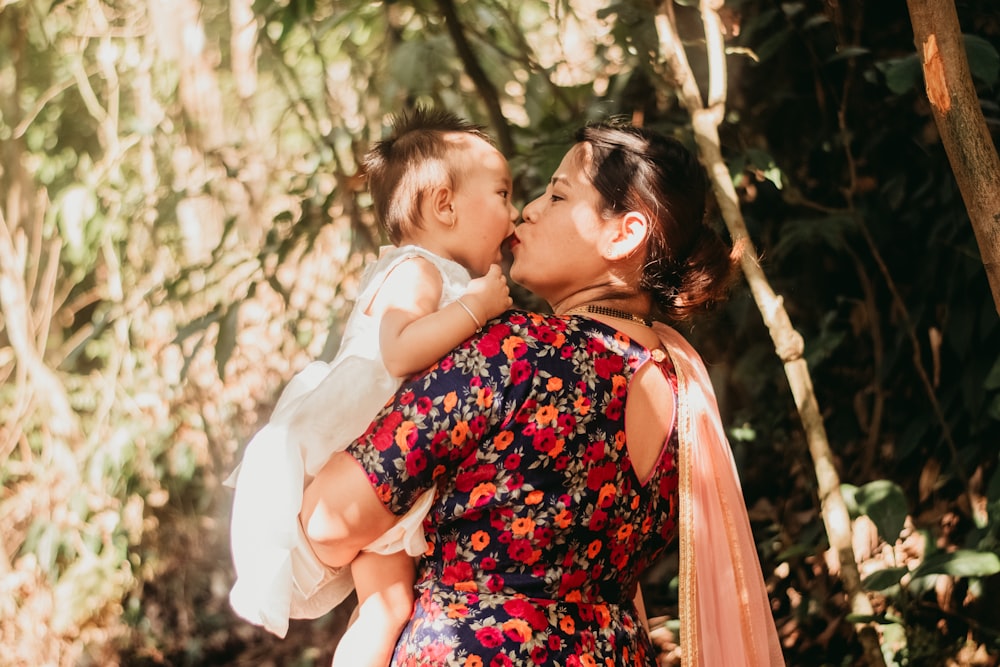 woman in red and black floral dress kissing girl in white dress