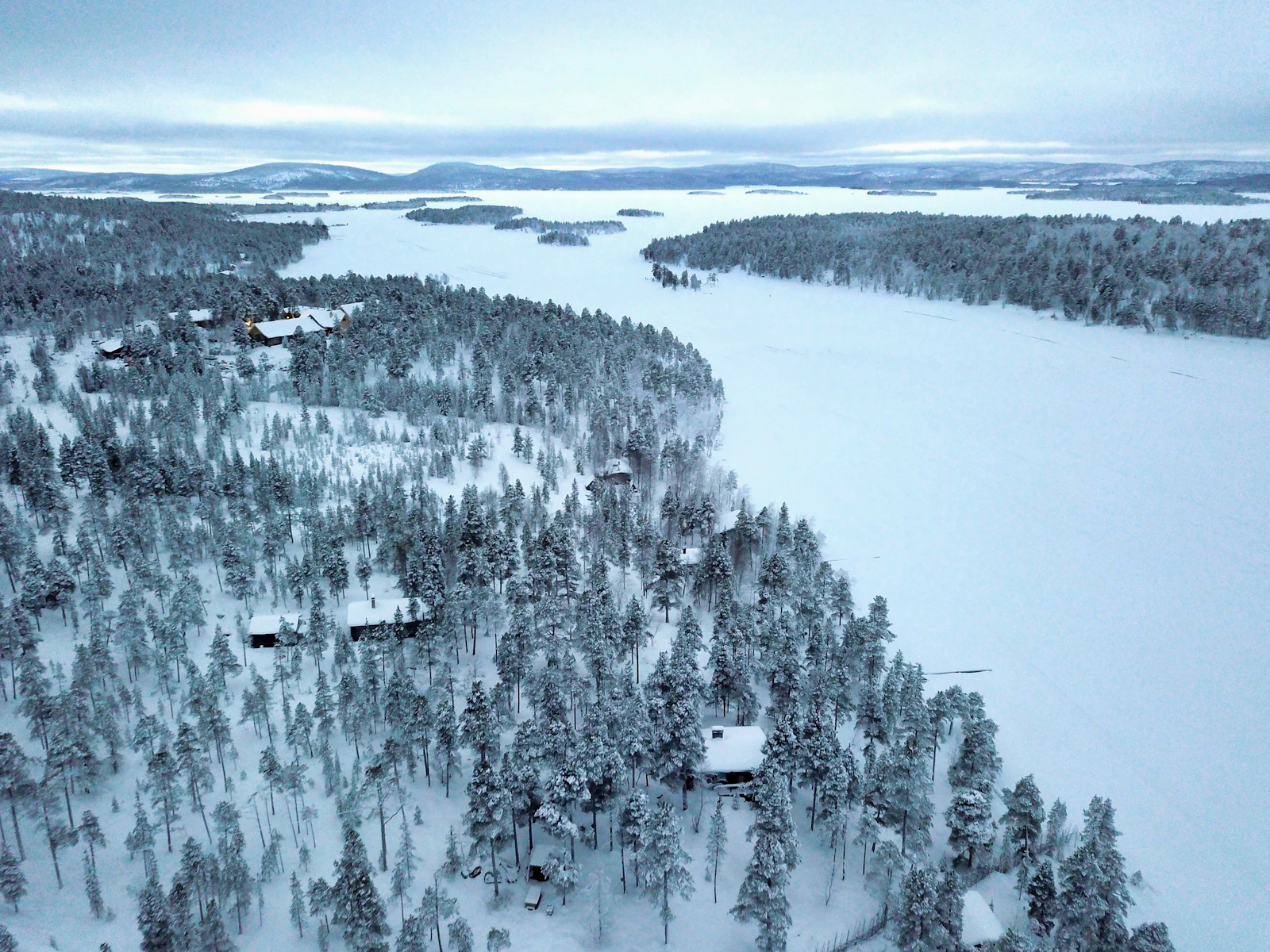Forêt enneigée et chalets au bord d’un lac gelé en Laponie finlandaise