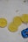 Several lemon slices arranged in a row on a light background with some brown stains nearby. A small blue toy car is positioned close to the lemon slices.
