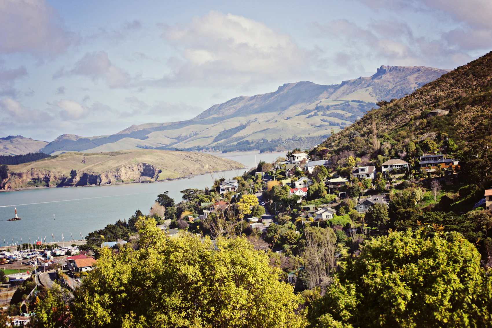 Houses beside calm water and green hills in the Canterbury region