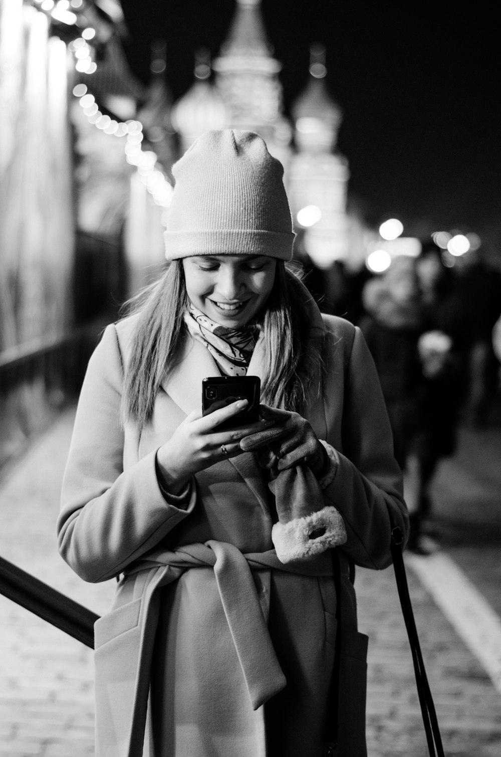 woman in knit cap and coat holding smartphone