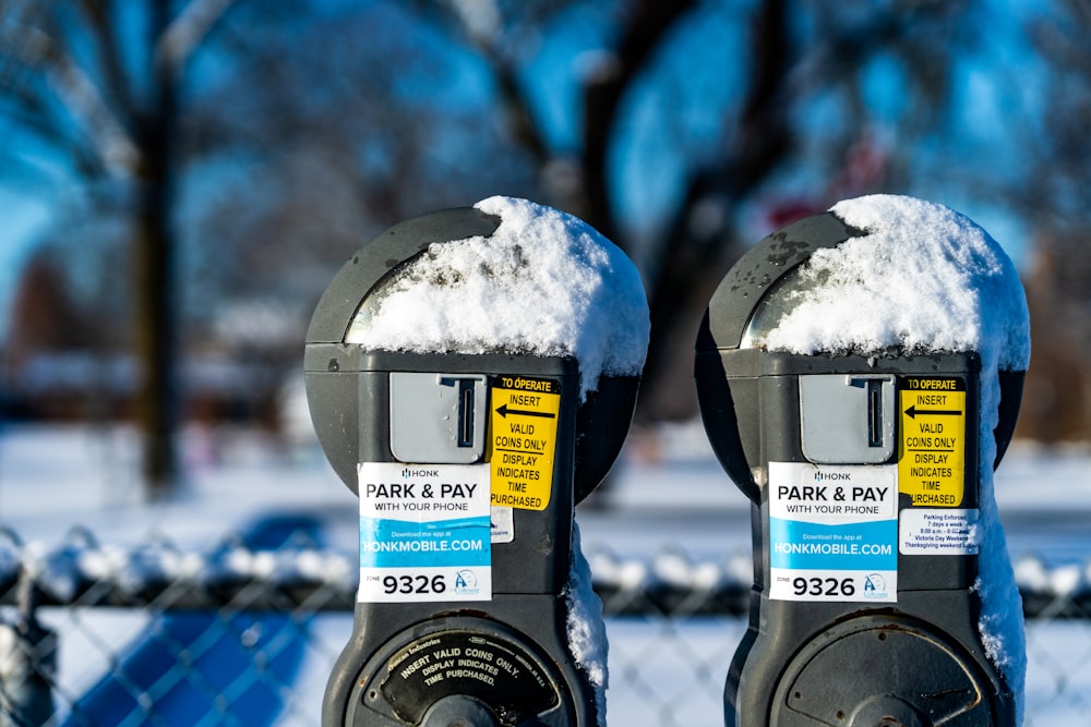 a parking meter covered in snow next to a fence