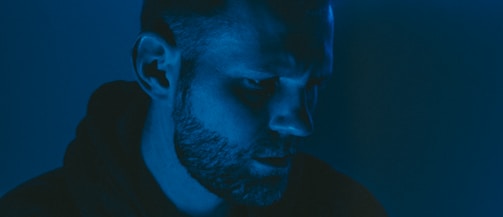 Close-up of an actor’s face half-lit by moody, blue-hued lighting with droplets of rain.
