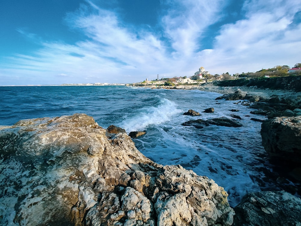 olas oceánicas rompiendo en la costa rocosa bajo un cielo nublado azul y blanco durante el día