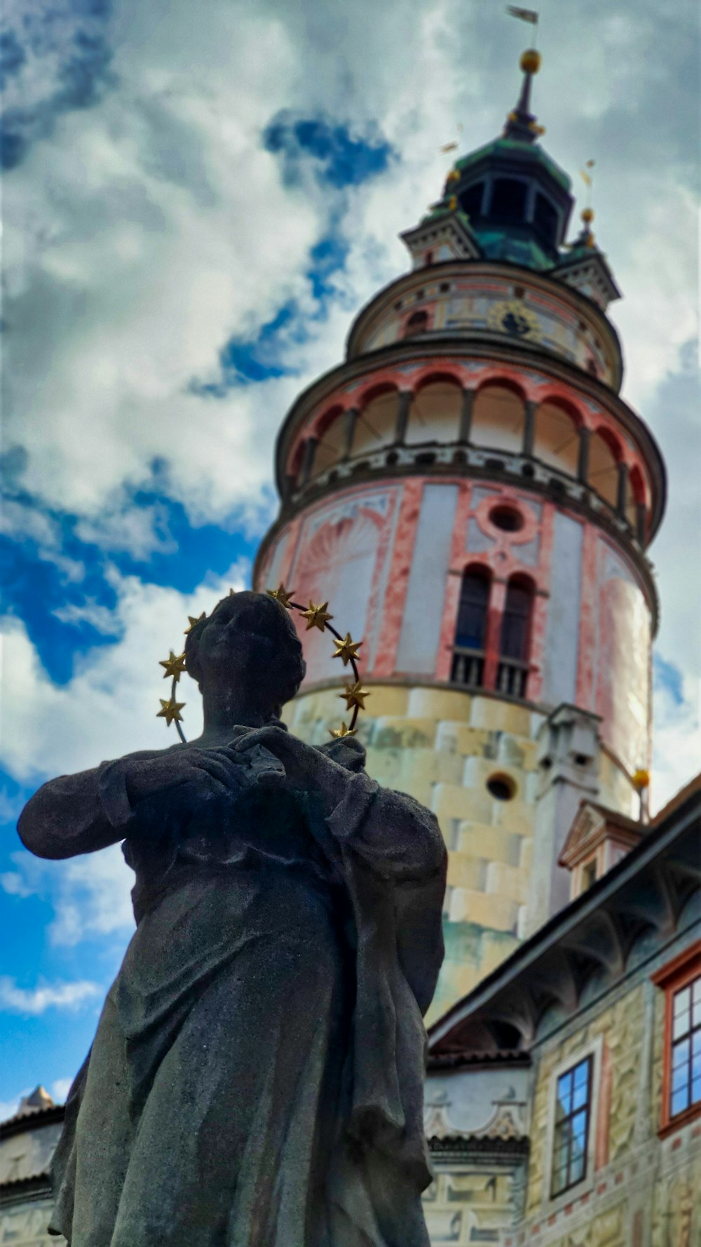 statue de l’homme près d’un bâtiment en béton blanc et brun sous un ciel nuageux bleu et blanc pendant