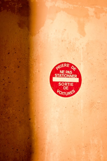 A red circular sign is mounted on a textured wall. The sign, which appears to be a parking-related warning in French, contrasts with the warm, earthy tones of the wall.