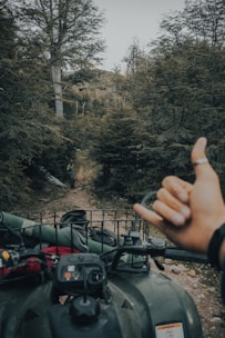 A compact trailer attached to an ATV, carrying hunting gear through a wooded trail.