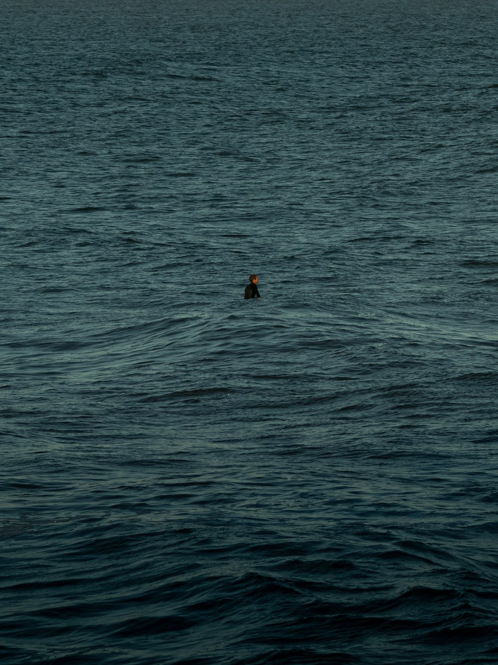 person in red shirt swimming on sea during daytime