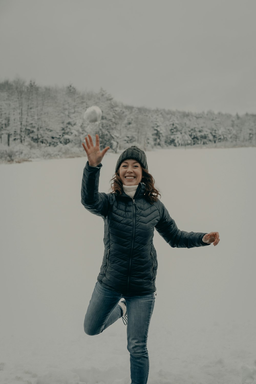 Frau in schwarzer Jacke und blauer Jeans steht tagsüber auf schneebedecktem Boden