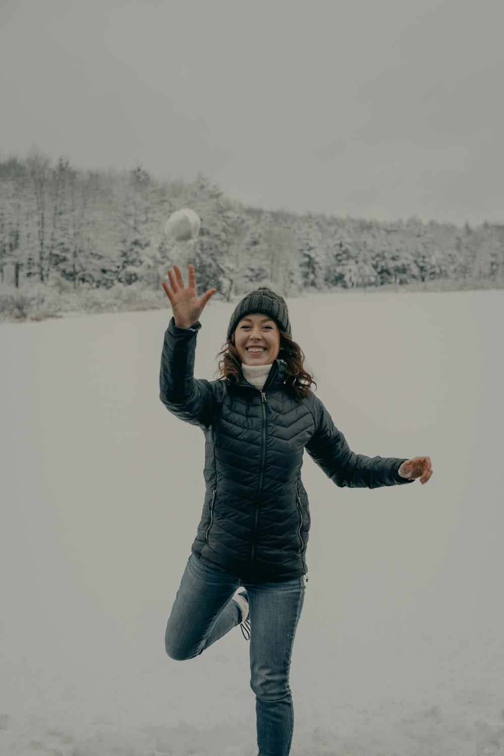 Mujer con chaqueta negra y jeans de mezclilla azul de pie en el suelo cubierto de nieve durante el día