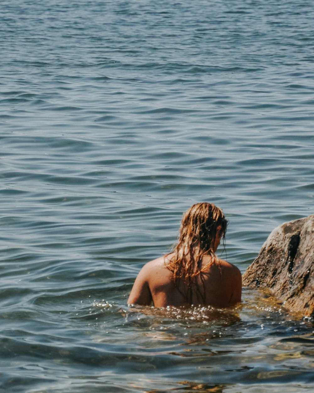 Frau im schwarzen Bikini sitzt tagsüber auf Felsen vor Gewässer