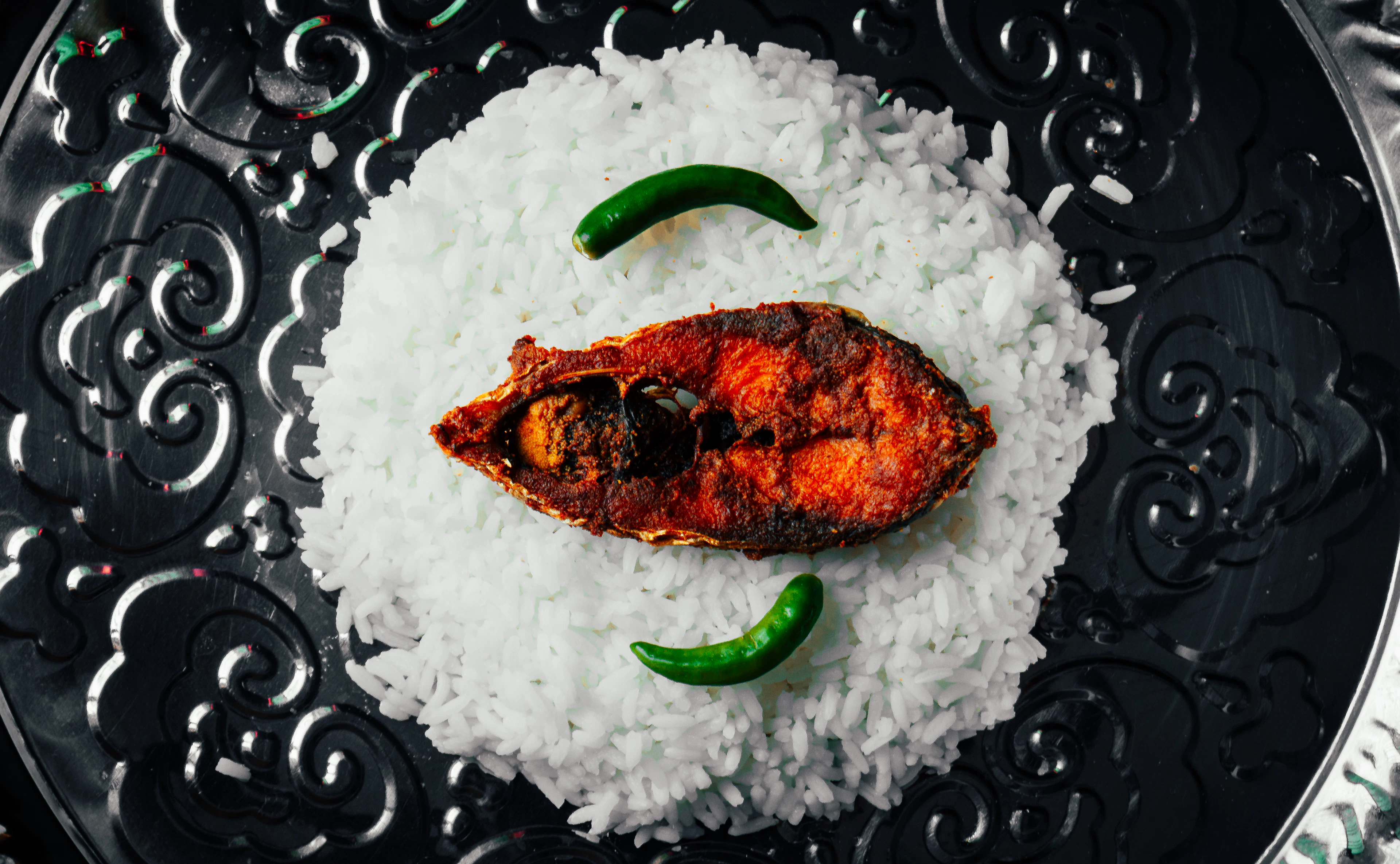 A whole spiced fish served over rice on an engraved platter, Goa