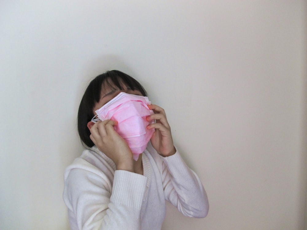 woman in white long sleeve shirt covering her face with pink textile