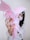 A person holds a bunch of pink medical masks in their hand, with the strings and pleats visible. The person is wearing a white top and a similar pink mask, partially covering their face. The background is plain and out of focus, emphasizing the masks.