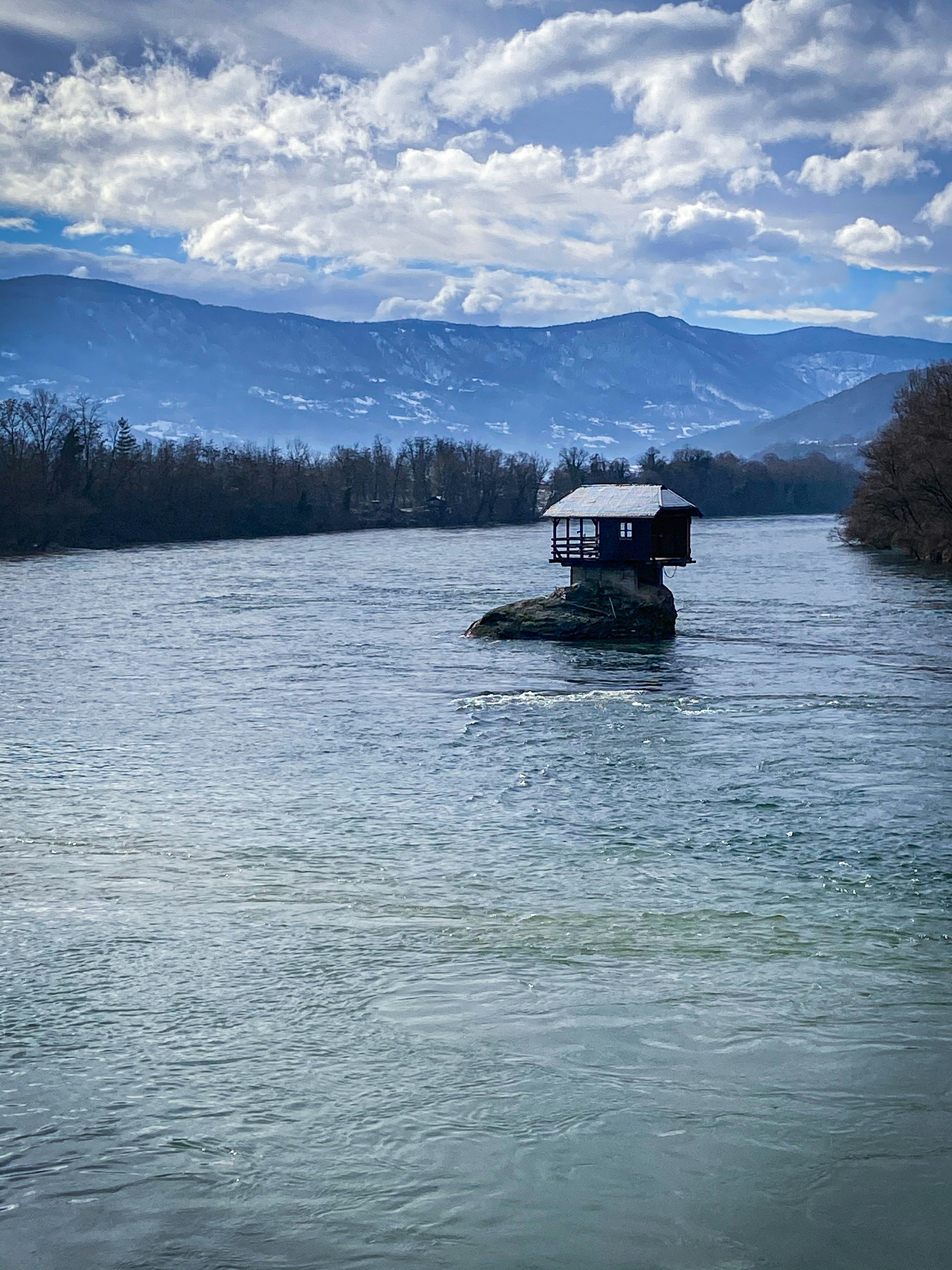 white and black house on body of water near green trees under white clouds and blue