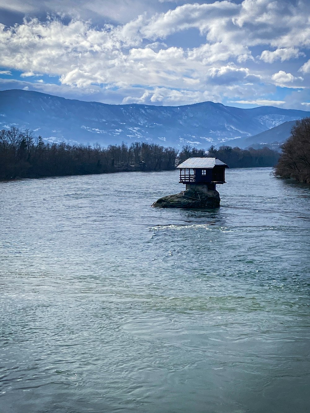 white and black house on body of water near green trees under white clouds and blue