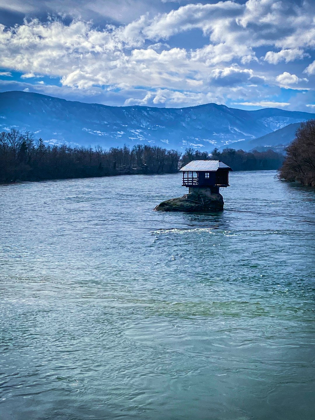 white and black house on body of water near green trees under white clouds and blue