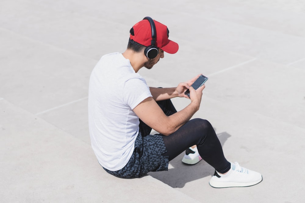 woman in white t-shirt and black pants sitting on floor using smartphone