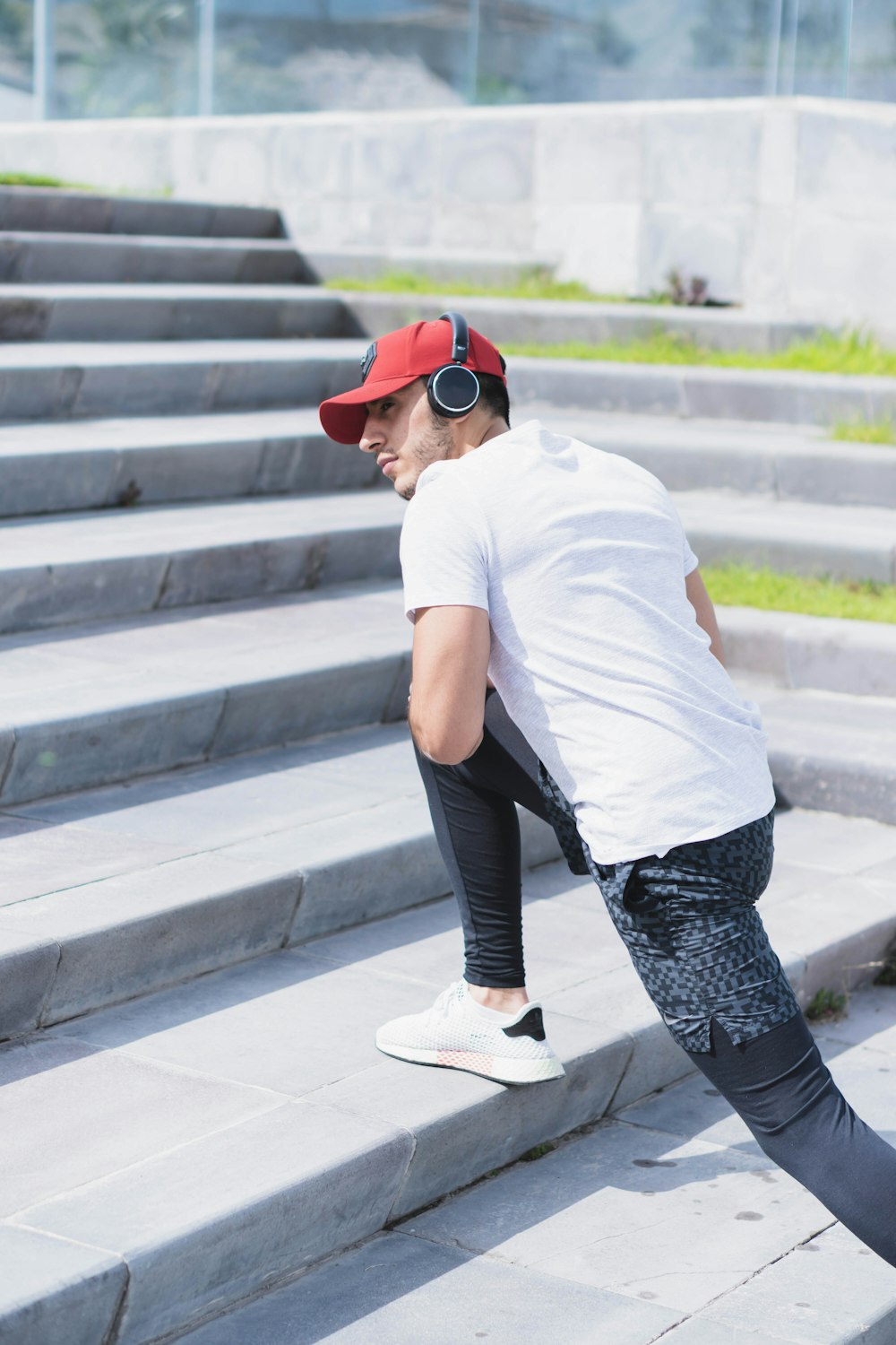 man in white t-shirt and black and white pants wearing white sneakers sitting on concrete
