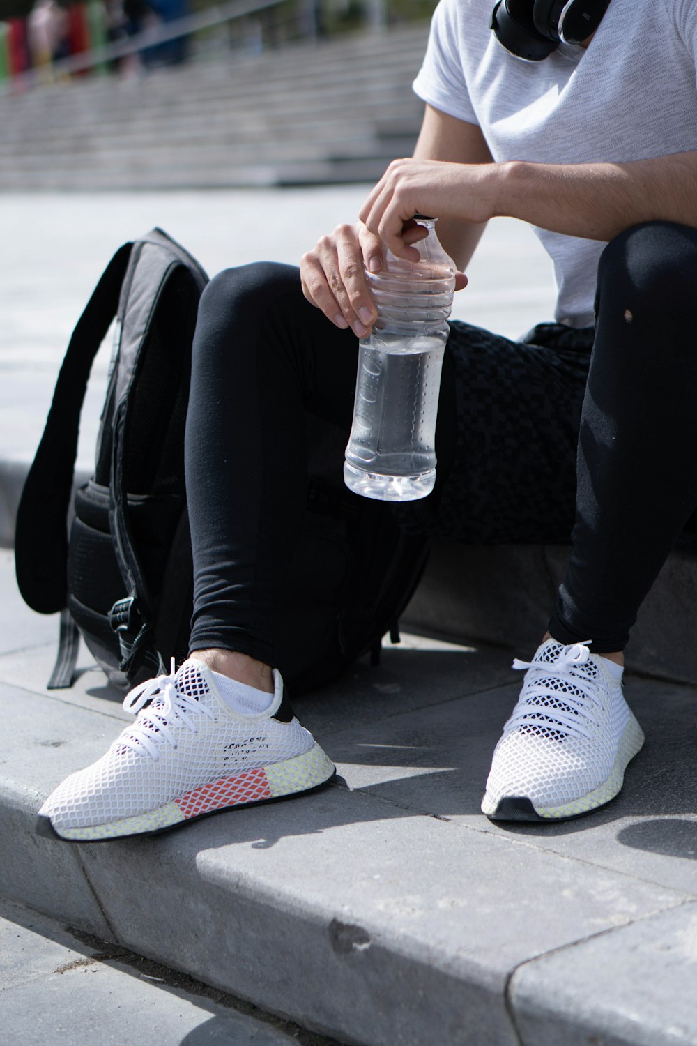 person in black pants and white nike sneakers holding clear plastic bottle