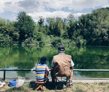 man in black shirt sitting on chair near lake during daytime