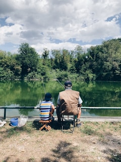 man in black shirt sitting on chair near lake during daytime