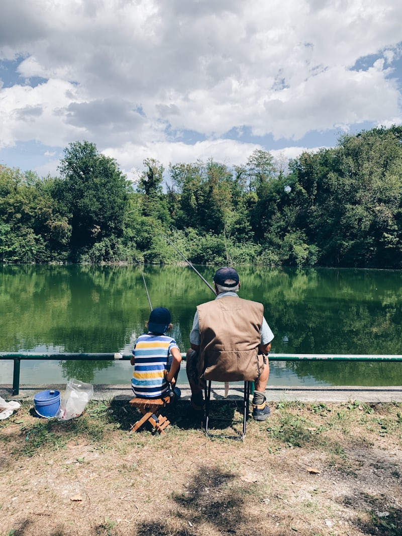 湖畔で魚釣りをするおじいさんと孫