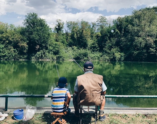 man in black shirt sitting on chair near lake during daytime